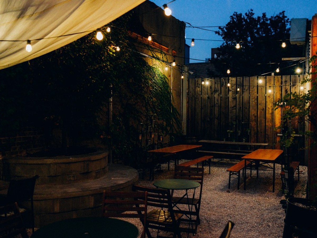 A terrace with festoon lights on poles, long trestle tables with linen and a canopy at one end.