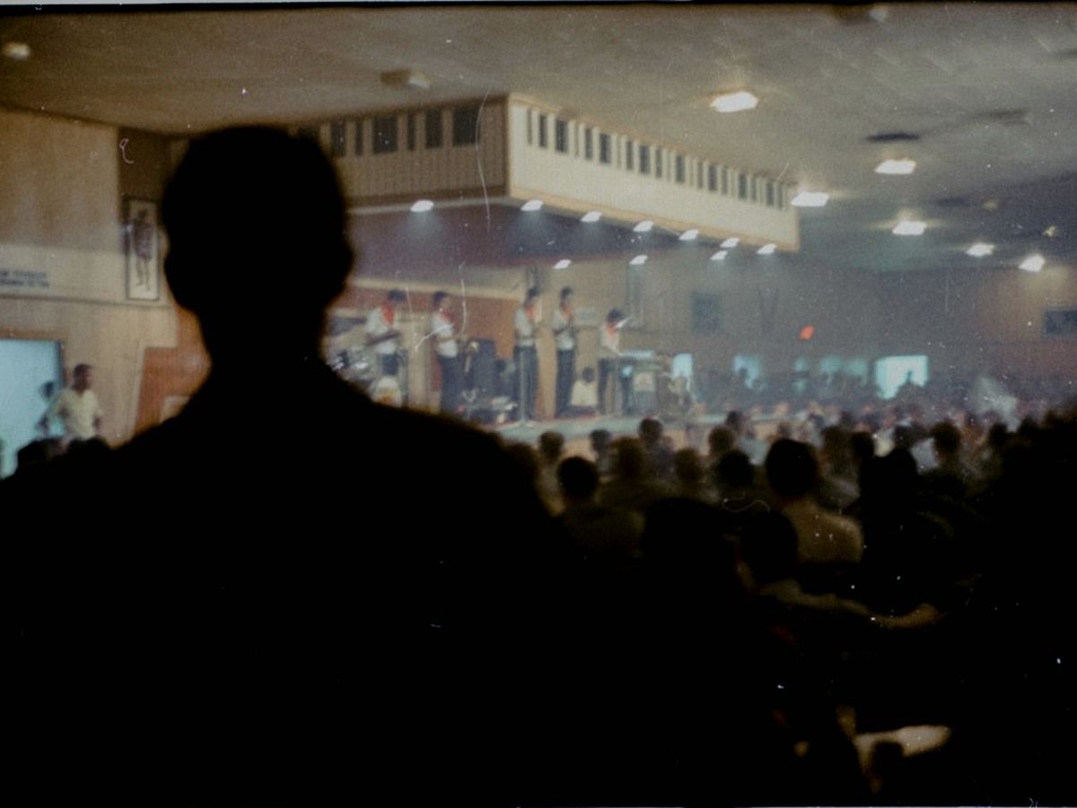 A hall with a large projection screen, a lectern on a low stage and round tables set for dinner.